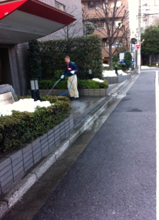 An apartment building caretaker attempts to hose away the last of the offending snow.
